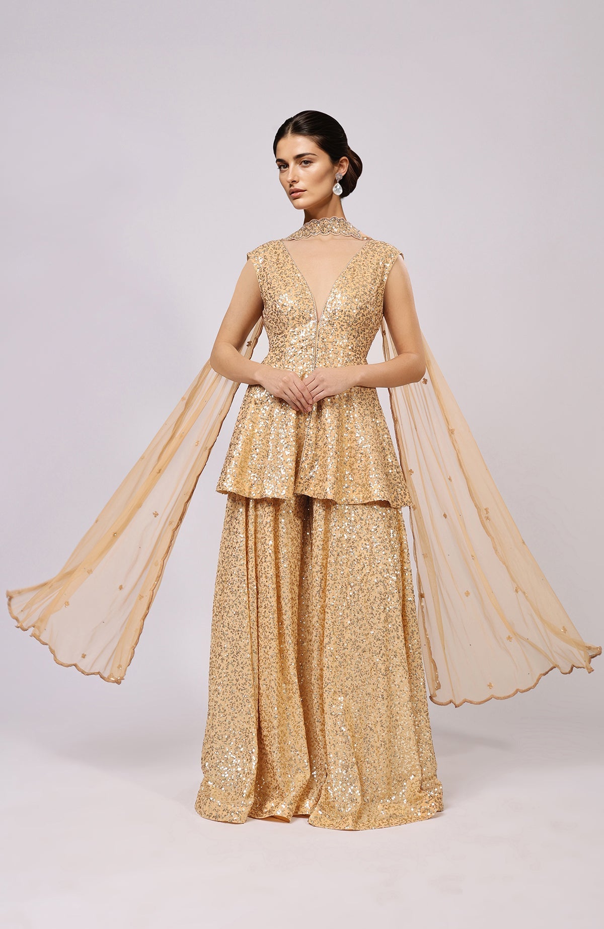 A model wears a gold sequin embroidered sharara set with a peplum top and flowing dupatta.