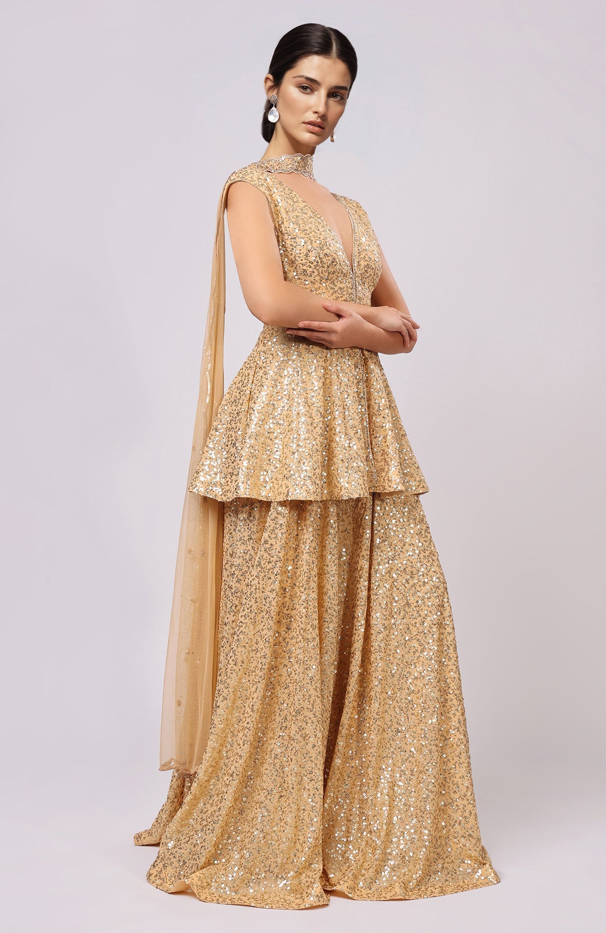 A model wears a gold sequin embroidered sharara set with a peplum top and dupatta.