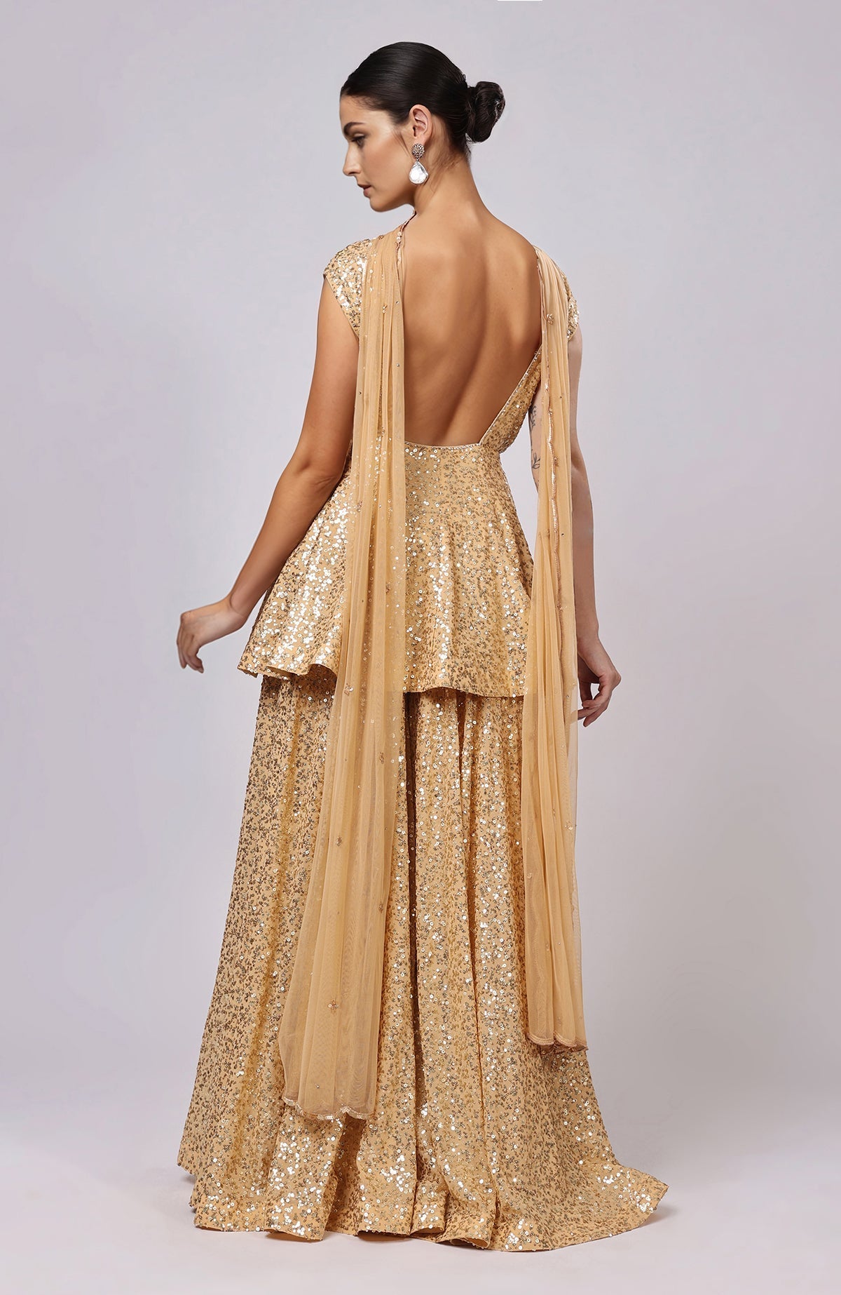 A woman models a gold sequin embroidered sharara set with a peplum top.