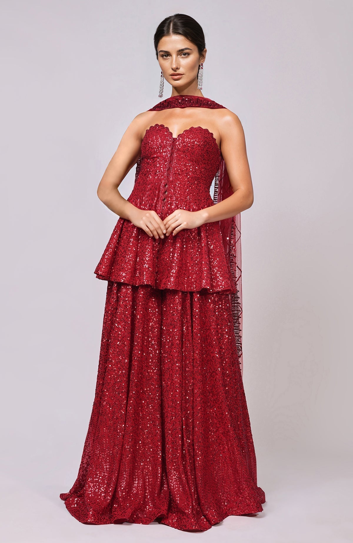 A model wears a red sequin embroidered sharara set with a peplum top and dupatta.