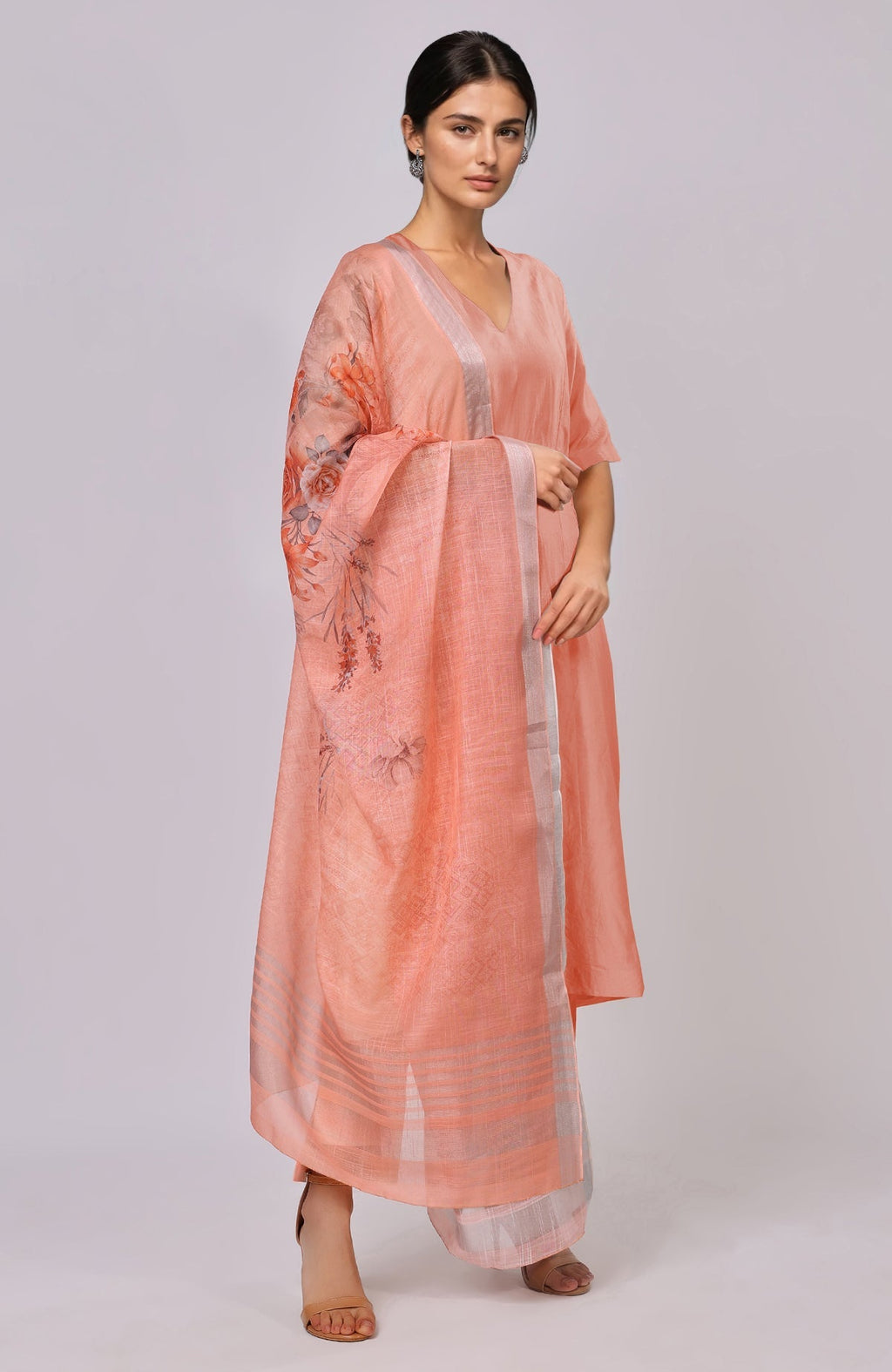 A woman models a peach floral linen dupatta with a matching suit and sandals.