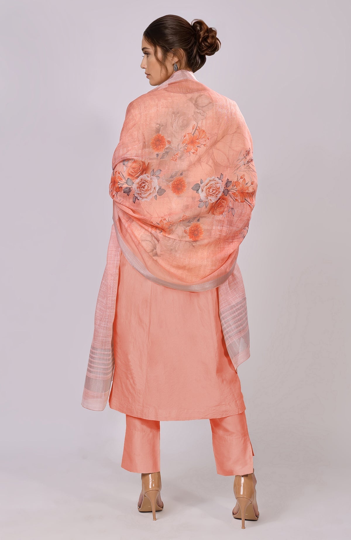 A woman models a peach floral linen dupatta draped over a matching suit.
