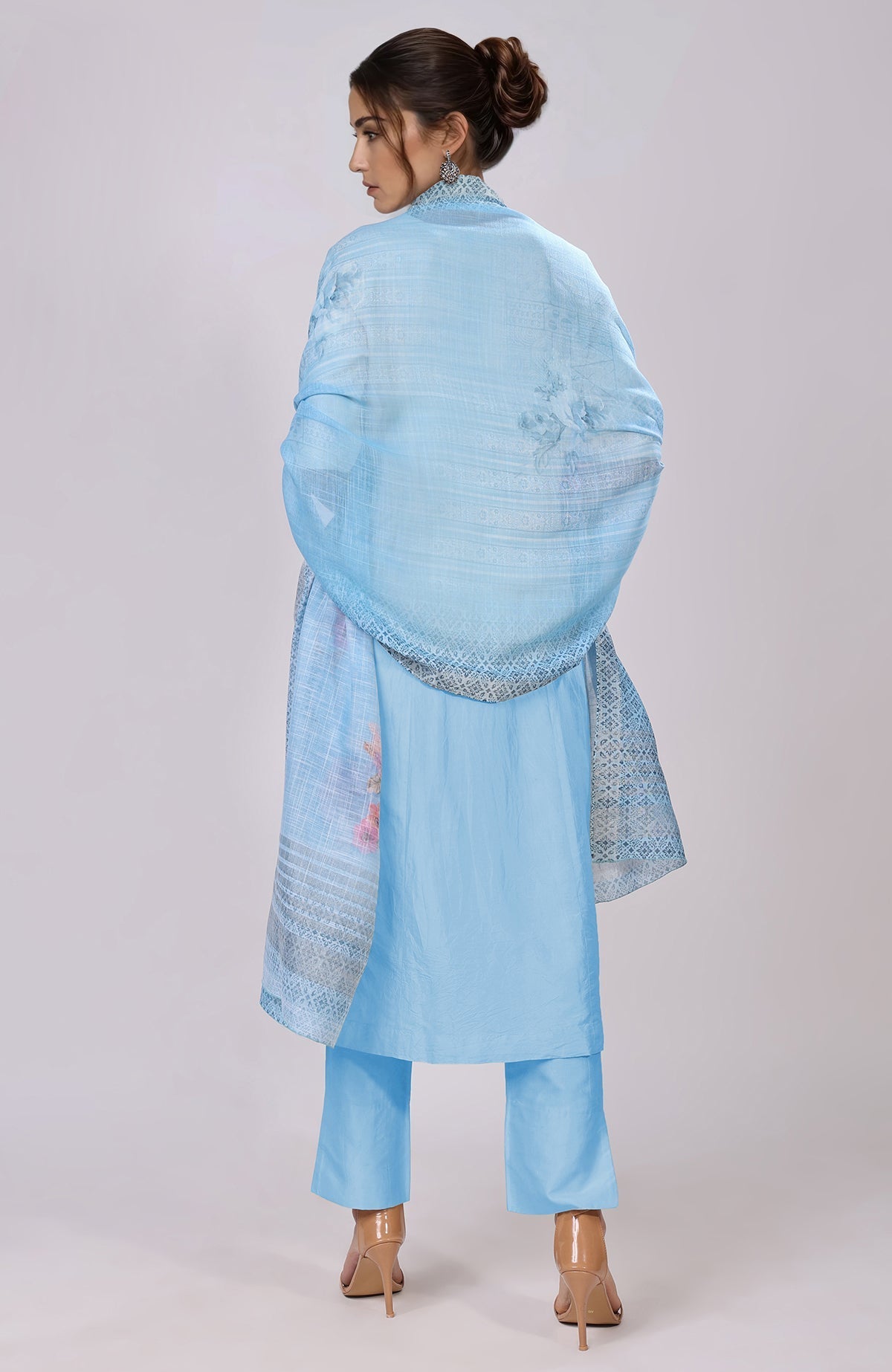 A woman models a sky blue floral linen dupatta with a matching suit and heels.