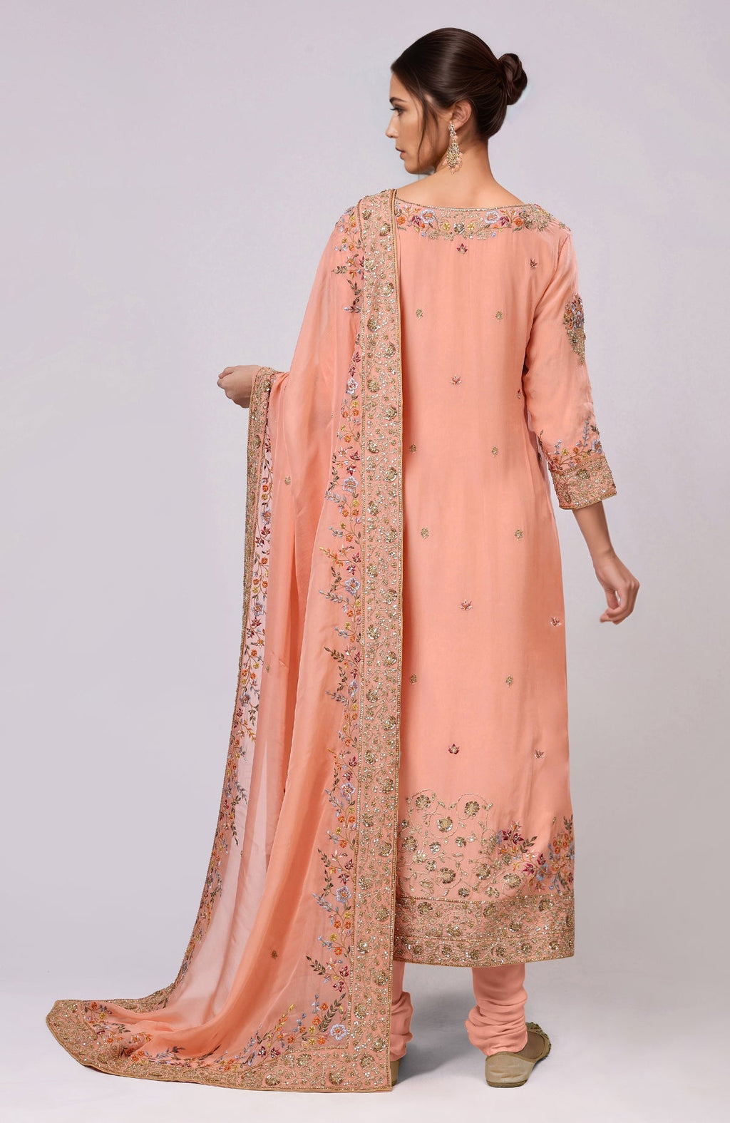 A woman models a salmon kurta set with intricate gold and colorful embroidery.