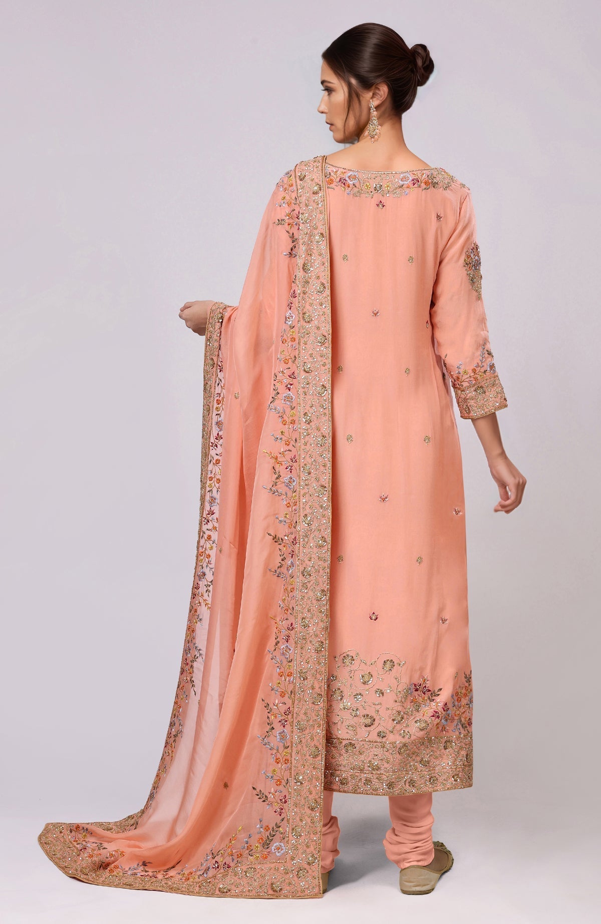 A woman models a salmon kurta set with intricate gold and colorful embroidery.