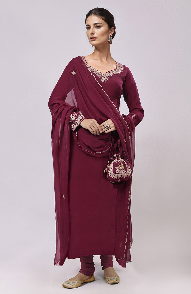 A woman models a burgundy kurta set with intricate embroidery and a matching potli bag.