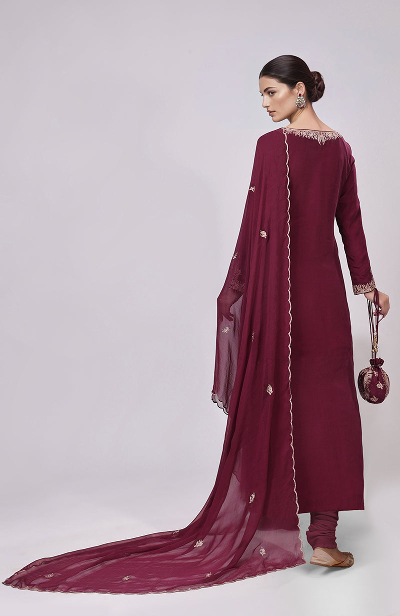 A woman models a burgundy Kashmiri Tilla Aari embroidered kurta set with a matching potli bag.