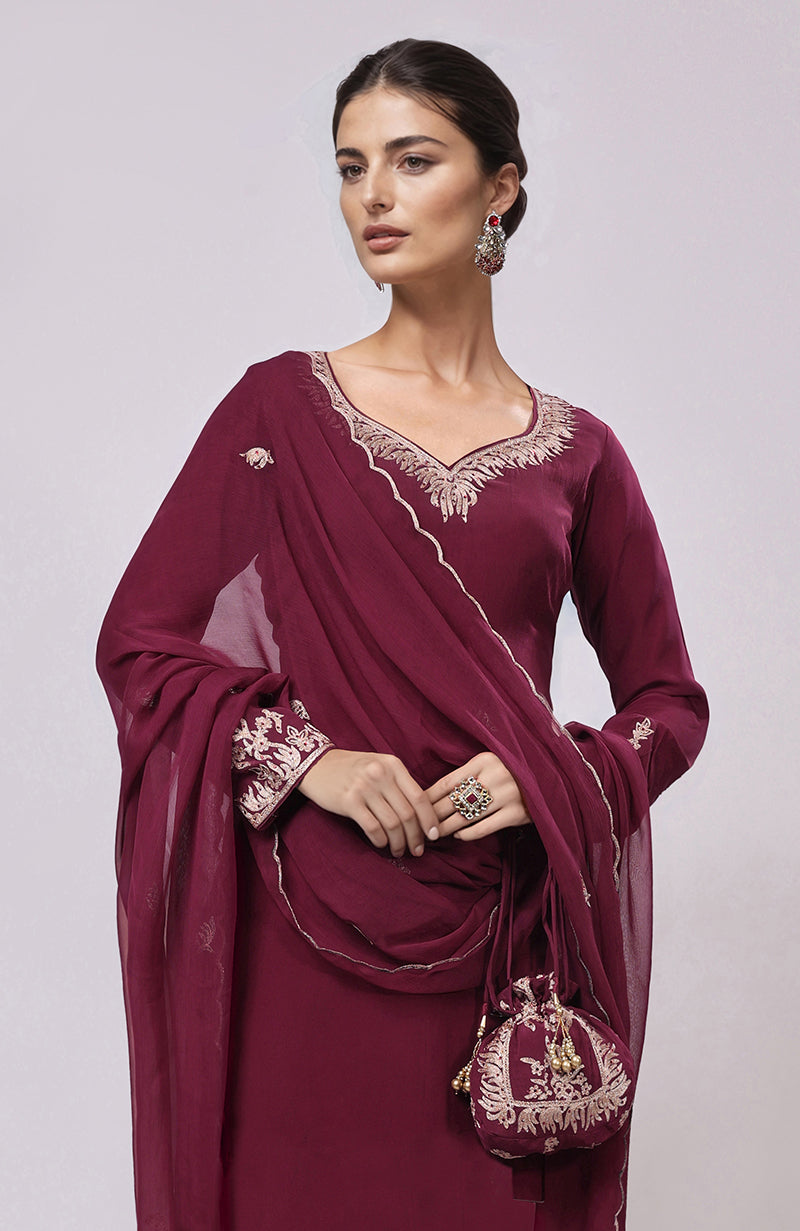 A woman models a burgundy Kashmiri Tilla Aari embroidered kurta set with a matching potli bag.