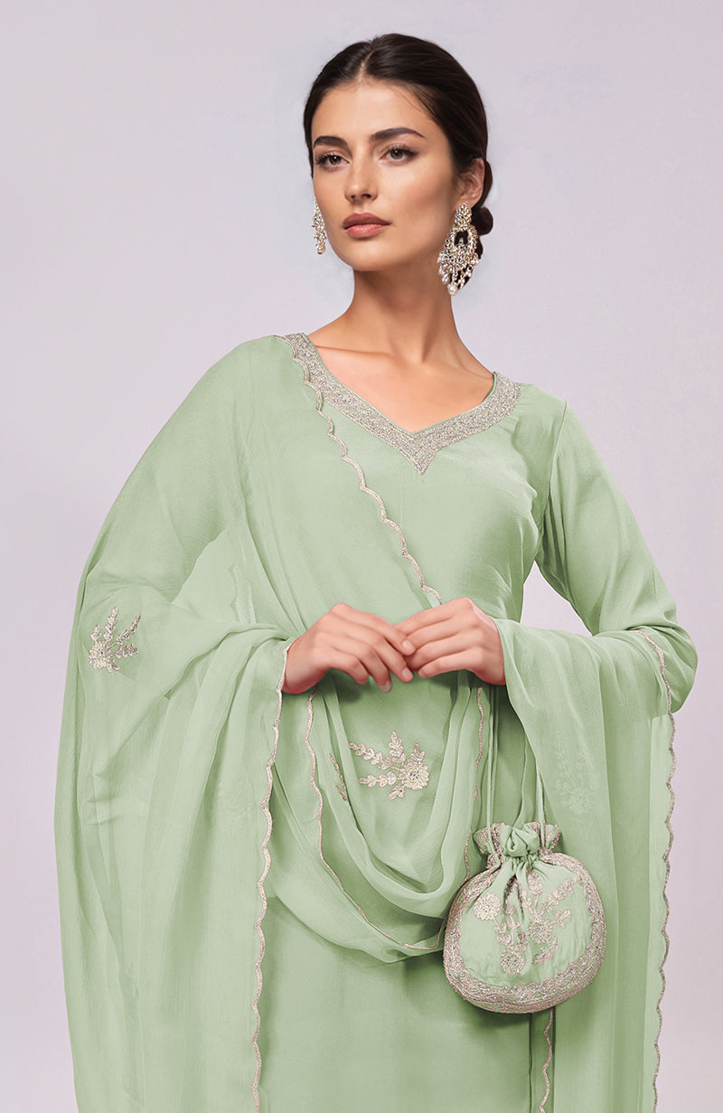 A woman models a sage green kurta set with intricate embroidery and a matching potli bag.
