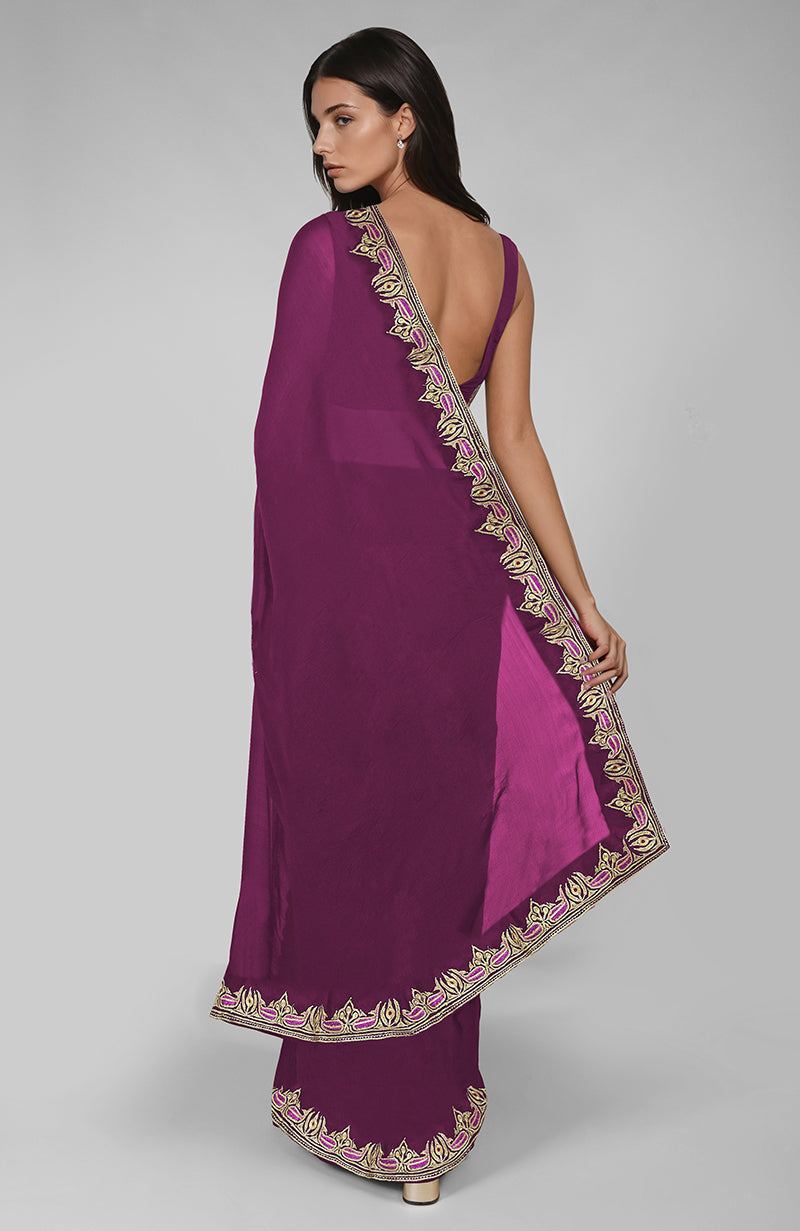 A woman models a peacock pink saree with gold and pink embroidered borders.