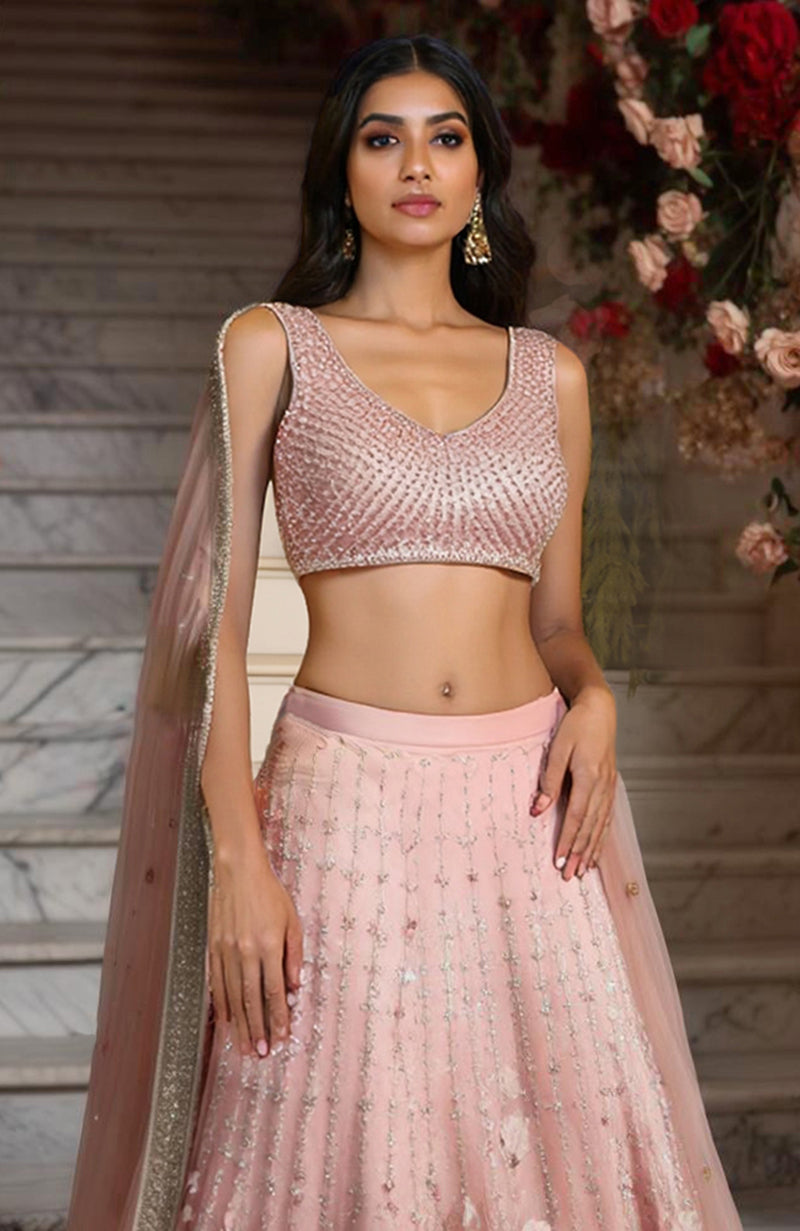 Blush pink lehenga set with sleeveless embellished blouse, floral embroidered skirt, and sheer dupatta.
