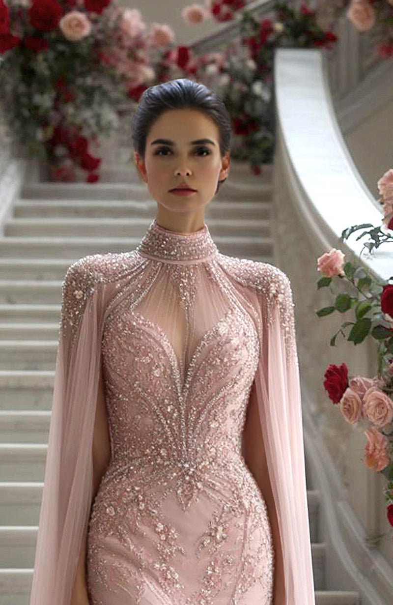 Blush pink gown with embroidered bodice, sheer high neck, long sleeves, and flowing cape overlay.