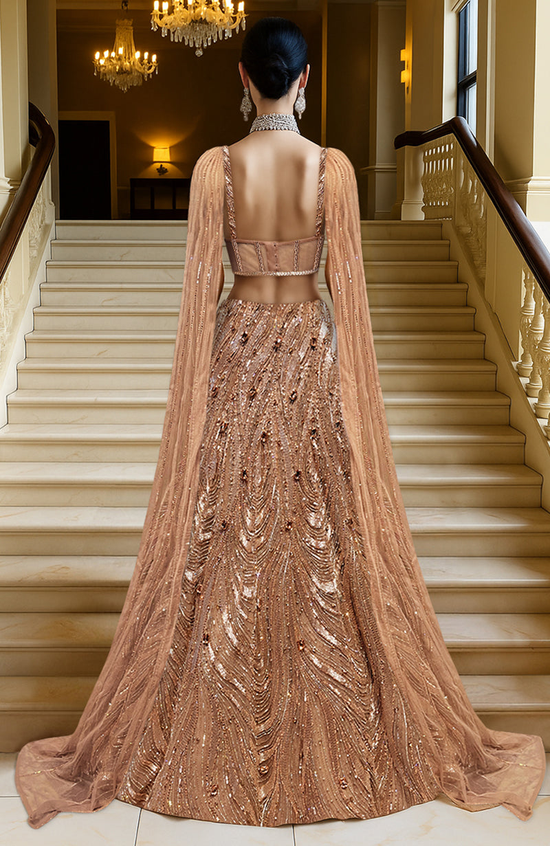 Rose gold lehenga set with hand embroidery, corset blouse, sheer cape, and flared skirt.