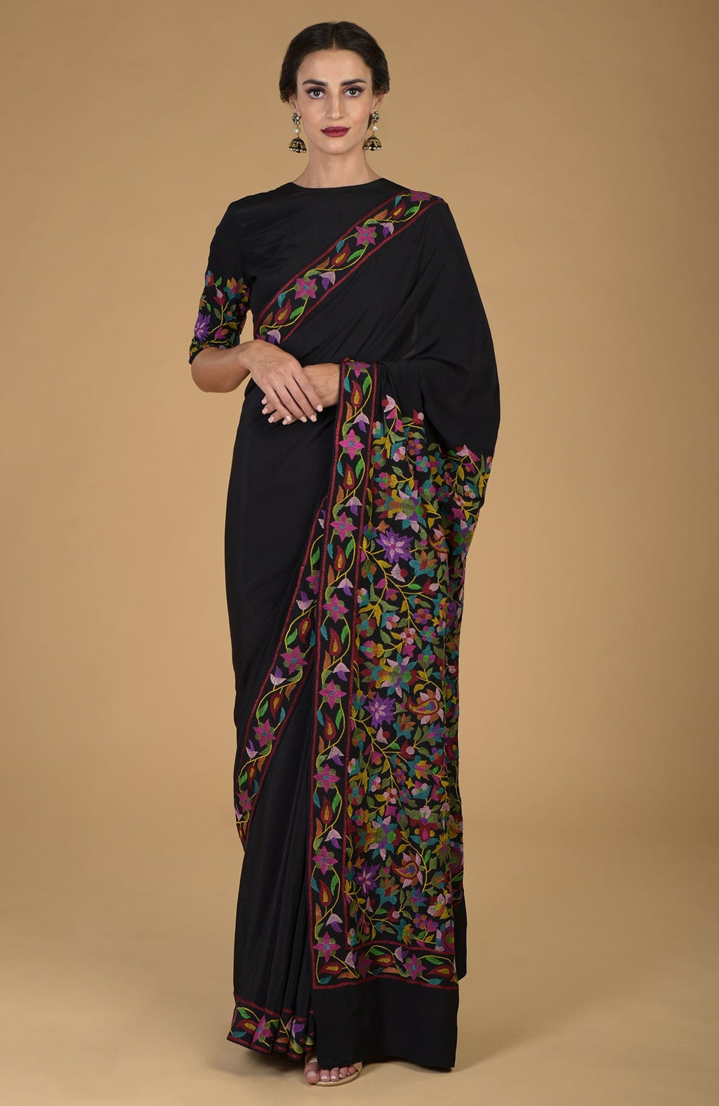 Woman in a black crepe silk saree with colorful floral Kani art embroidery.