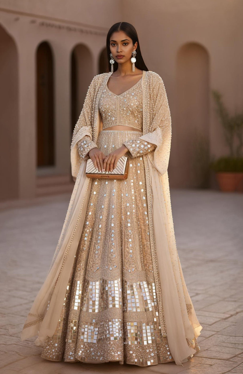 Champagne lehenga set with hand-embroidered mirrors, sequins, pearls, and sheer cape jacket.