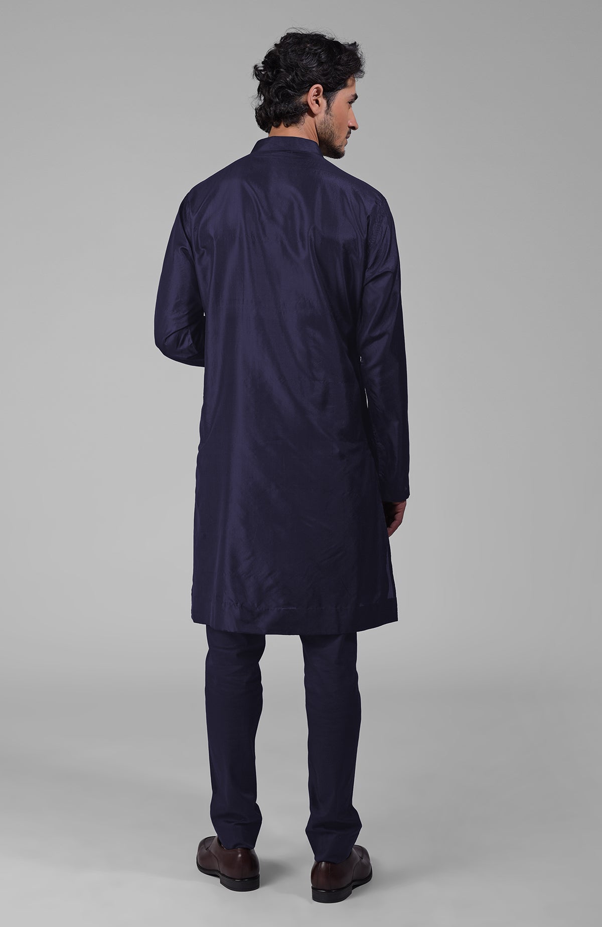 A man from behind wearing an ink blue silk kurta with floral embroidered placket detail.
