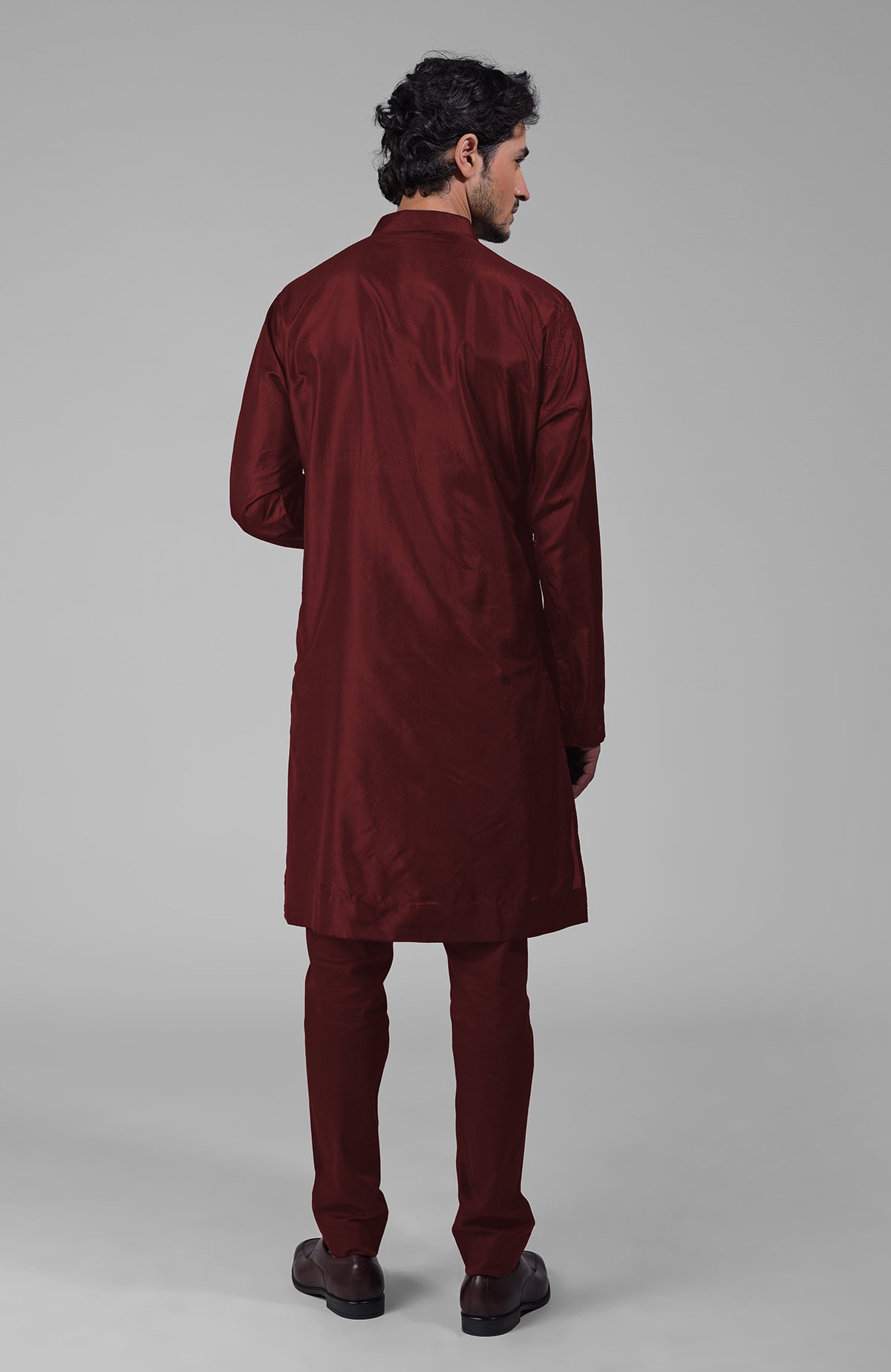 A man from behind wearing a maroon silk kurta and matching pants with brown shoes.