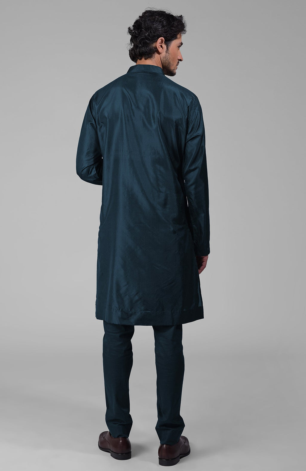 A man from behind wearing a teal silk kurta and matching pants with brown shoes.