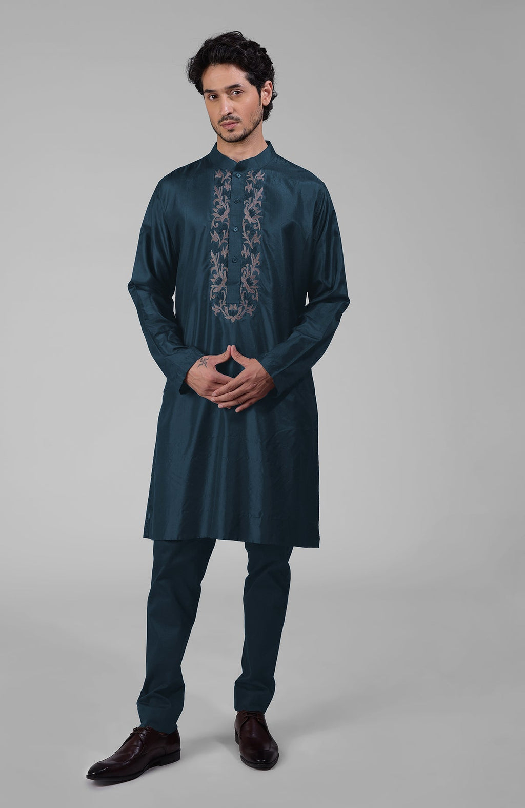A man models a dark teal silk kurta with floral embroidered placket and matching pants.