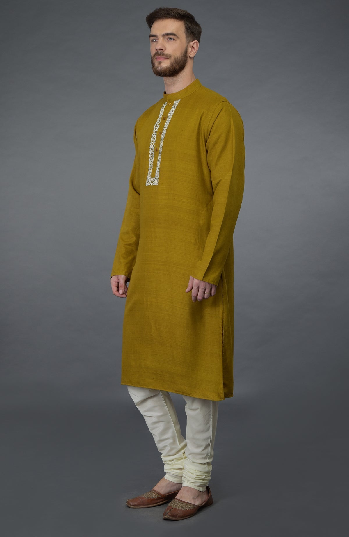 A man models a mustard pure silk kurta with an embroidered placket and ivory churidars.