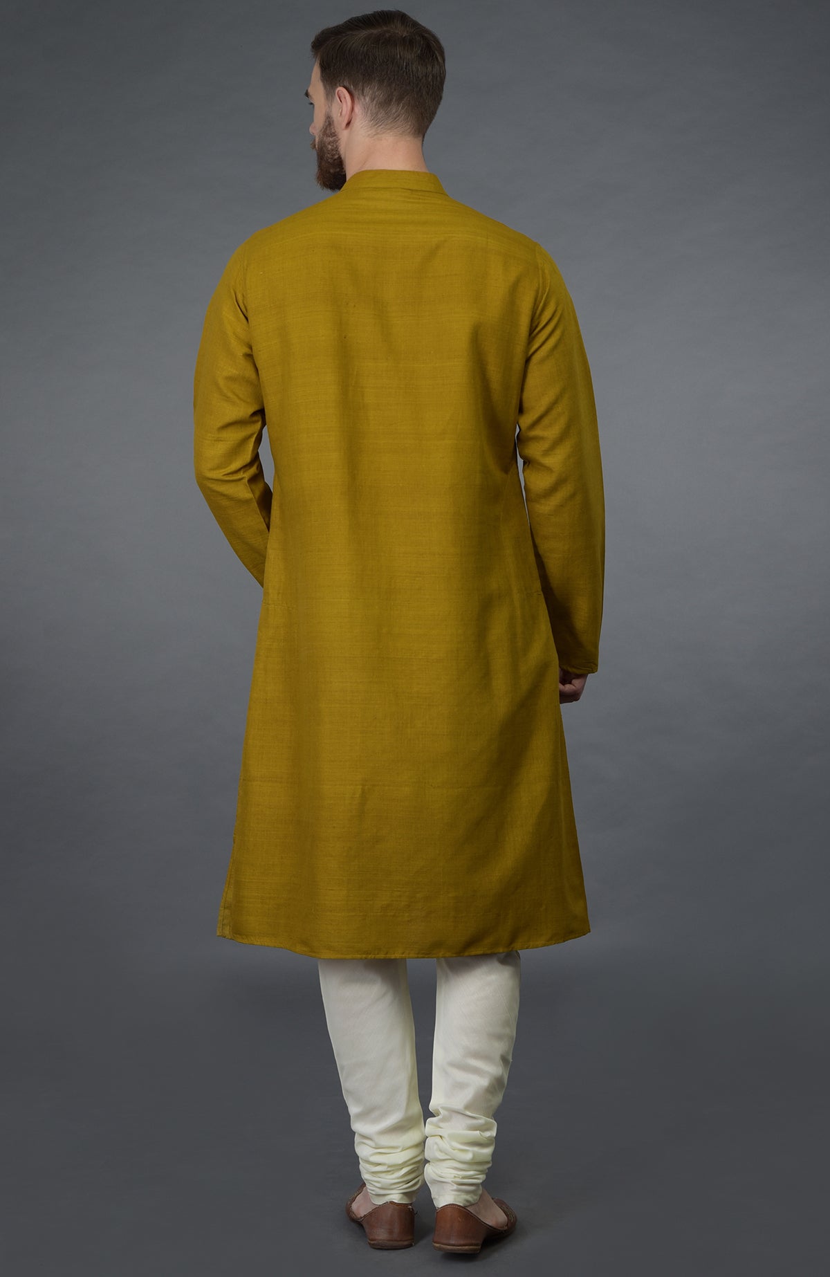 A man from behind wears a mustard pure silk kurta and ivory churidar.