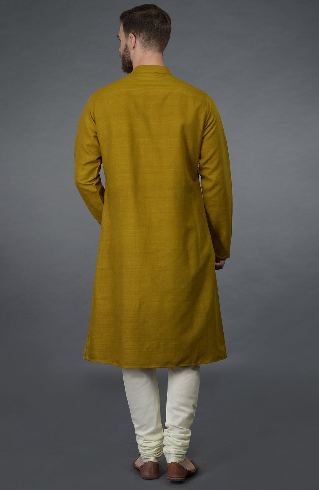A man from behind wears a mustard silk kurta and ivory churidar pants.
