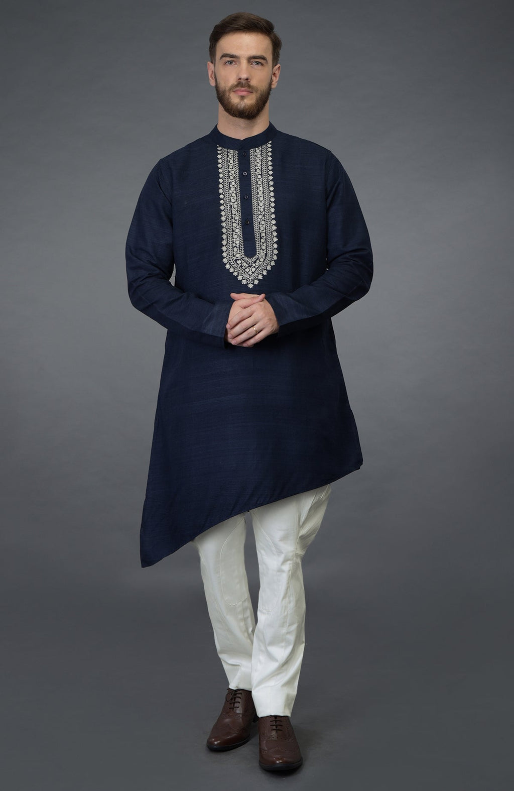 A man models a navy blue asymmetric kurta with silver tilla embroidery and white pants.
