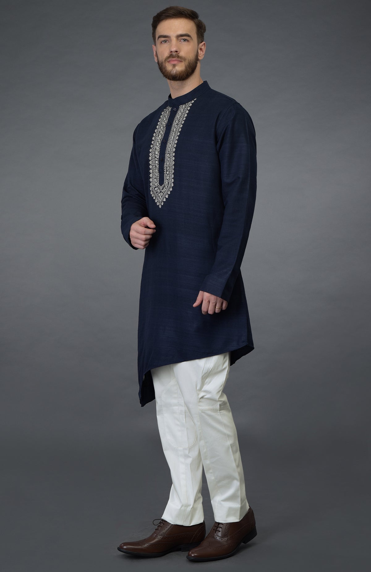 A man models a navy blue asymmetric kurta with silver embroidery and white breeches.