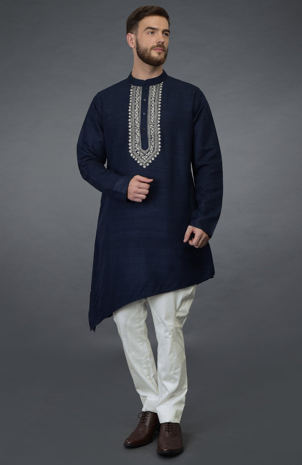 A man models a navy blue asymmetric kurta with silver tilla embroidery and white pants.