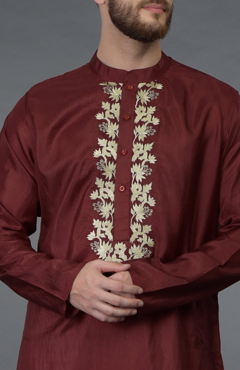 A man in a burgundy silk kurta with gold floral tilla embroidery.