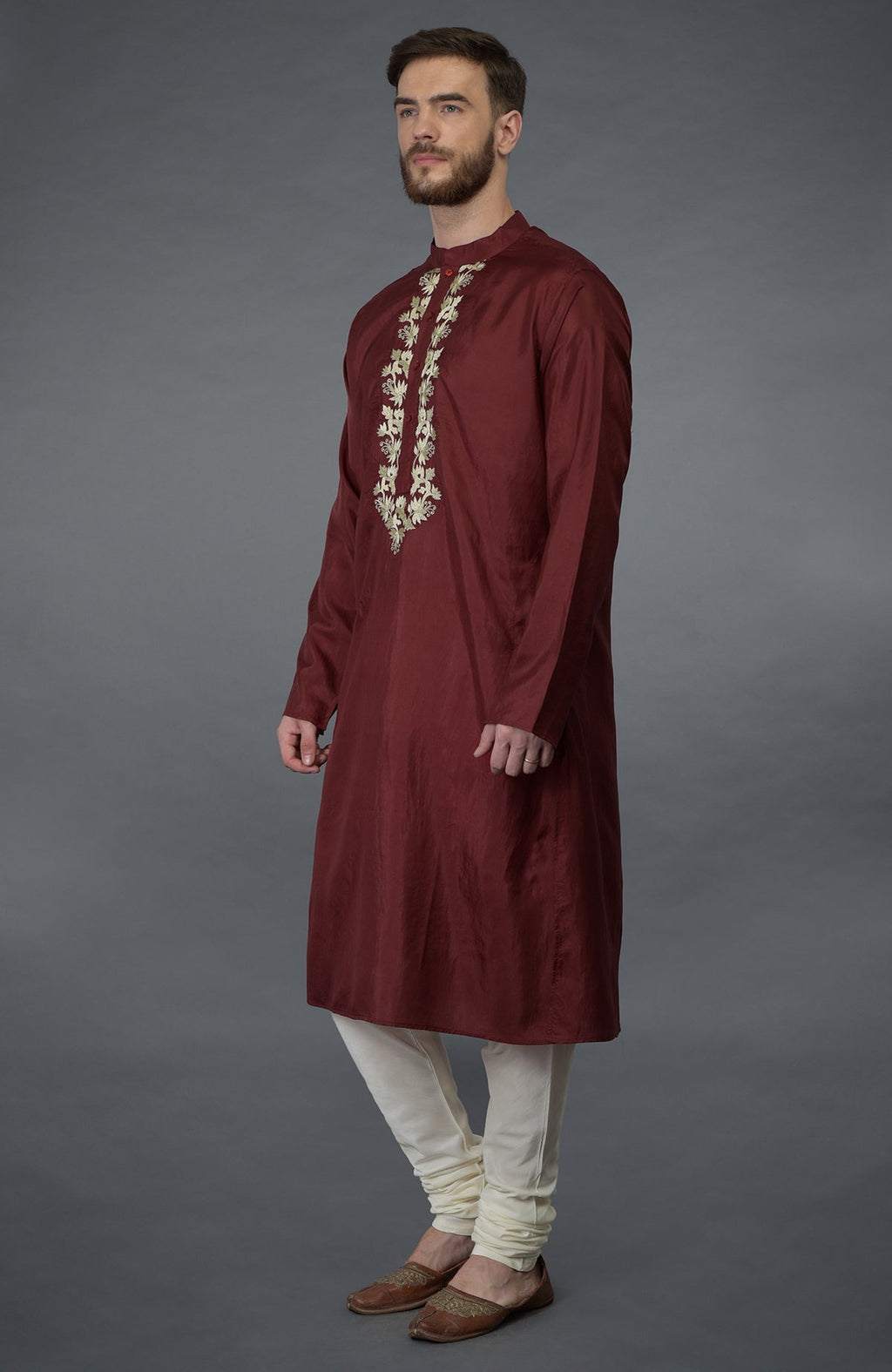 A man models a burgundy silk kurta with gold tilla embroidery and ivory churidars.