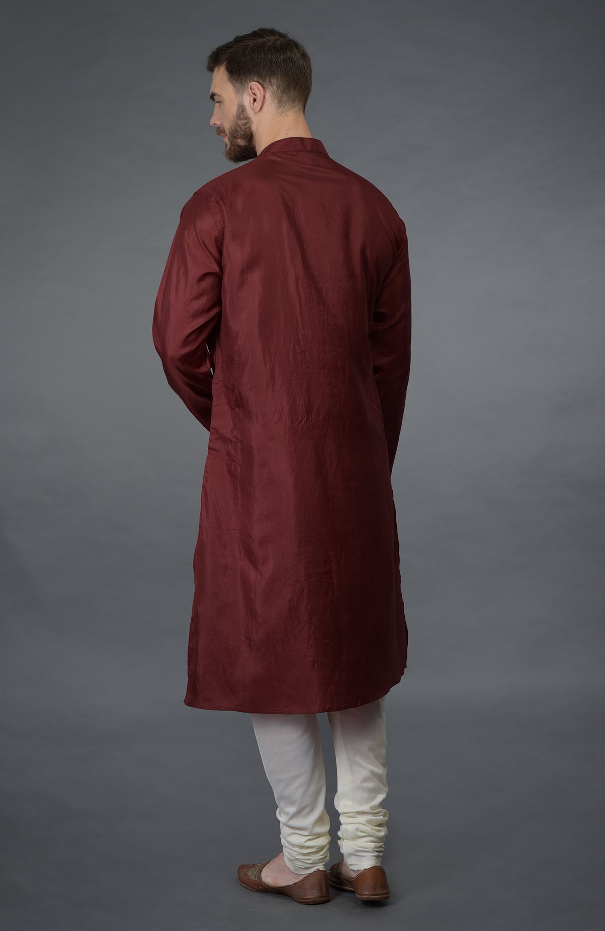 A man from behind wears a burgundy silk kurta and ivory churidar pants.