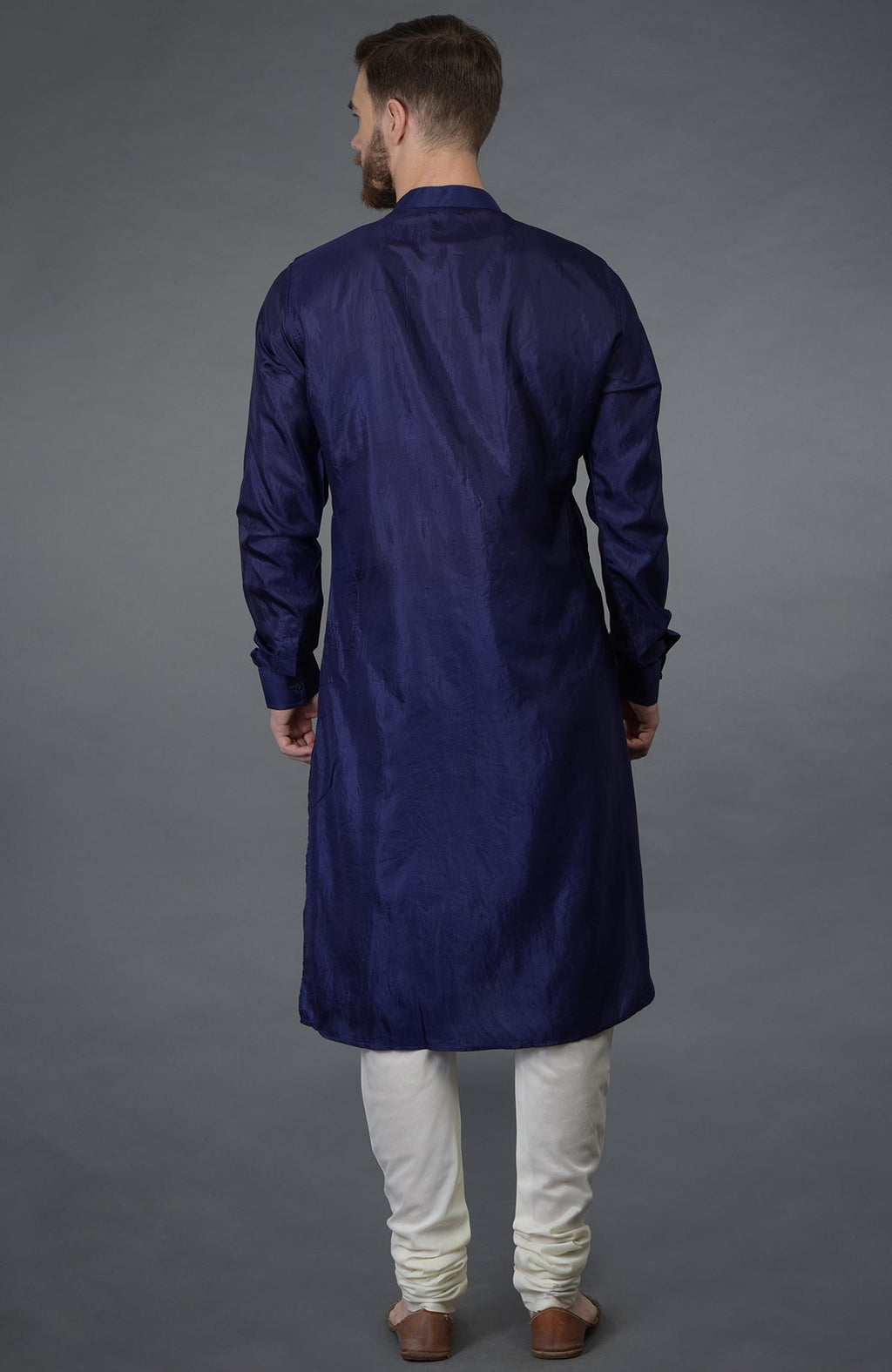 A man from behind wears an ink blue silk kurta and ivory churidar pants.