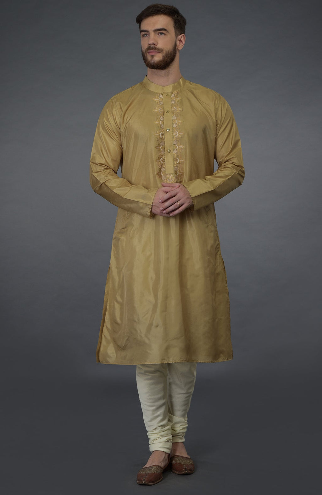 A man models a gold embroidered silk kurta set with ivory churidars and brown juttis.