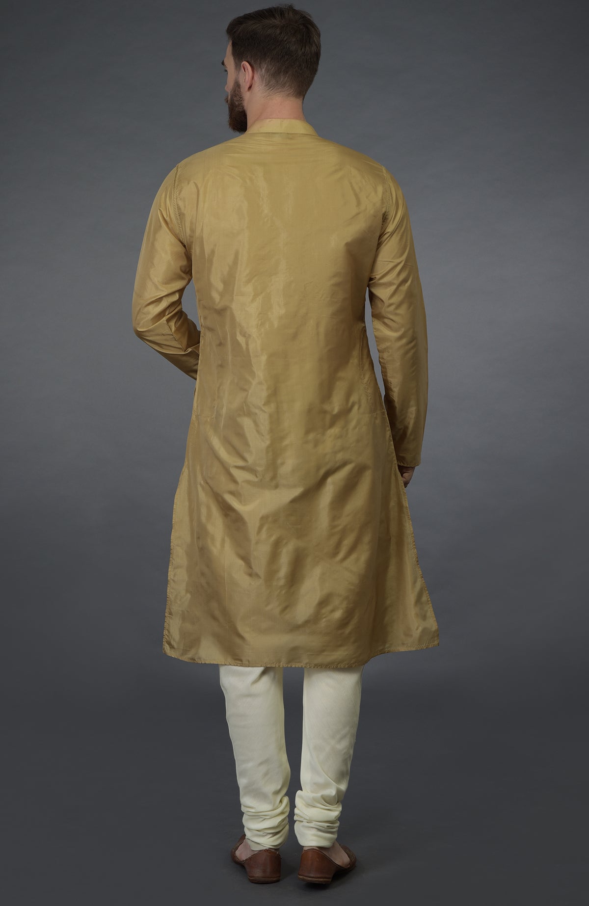 A man from behind wears a gold silk kurta and ivory churidar pants.