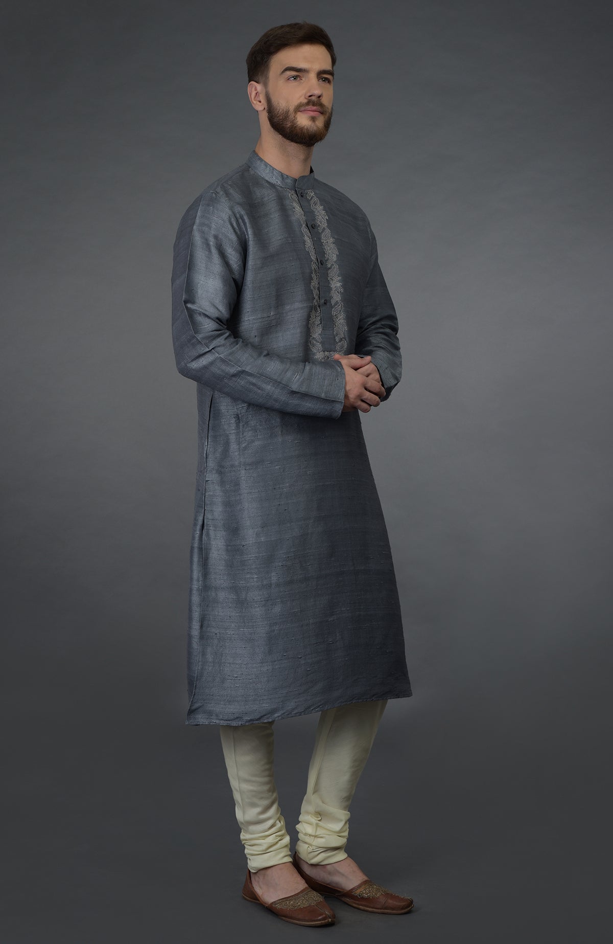 A man in a grey embroidered silk kurta and ivory churidar pants.
