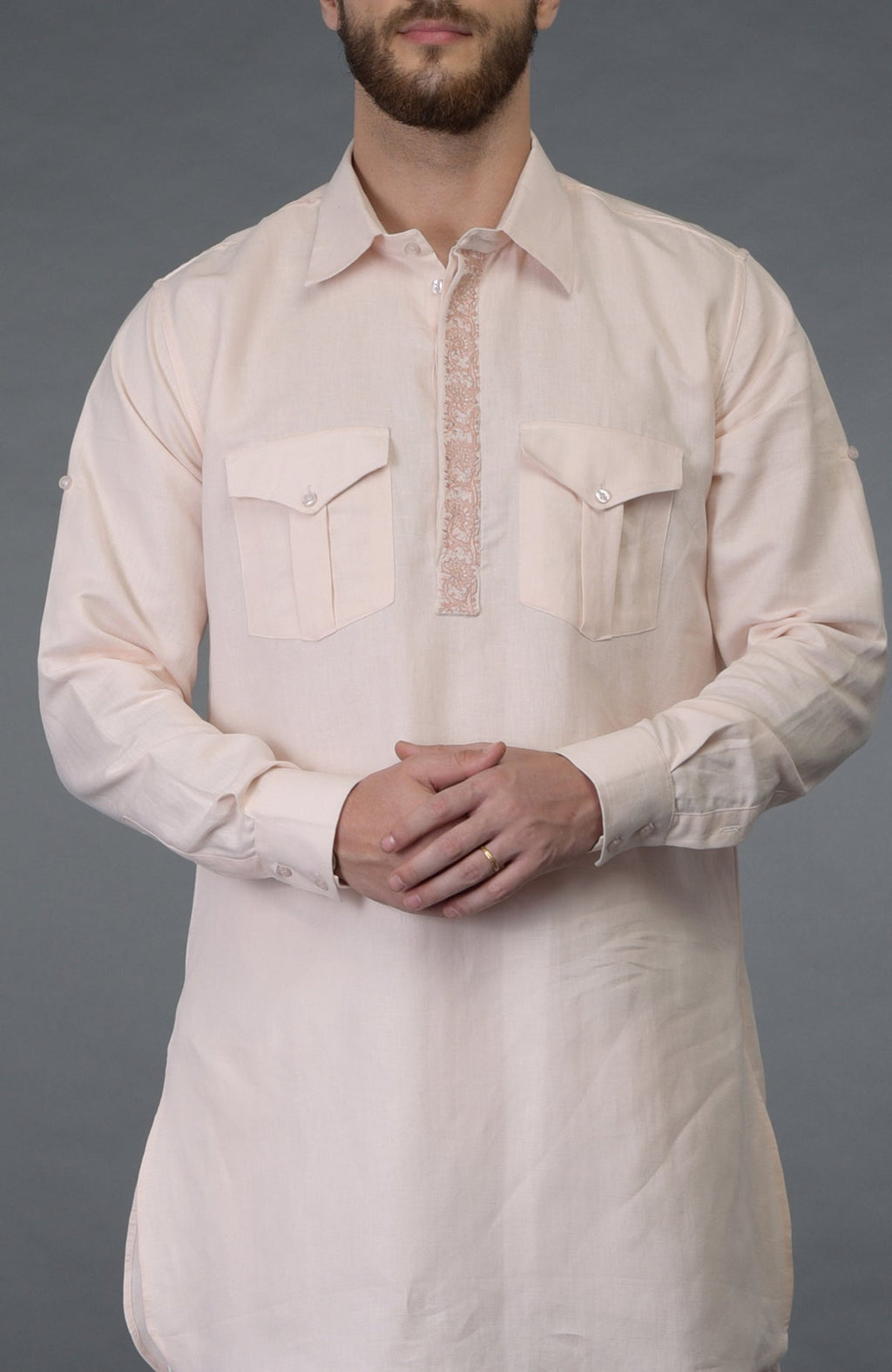 A man wears a baby pink linen kurta with embroidered placket and chest pockets.