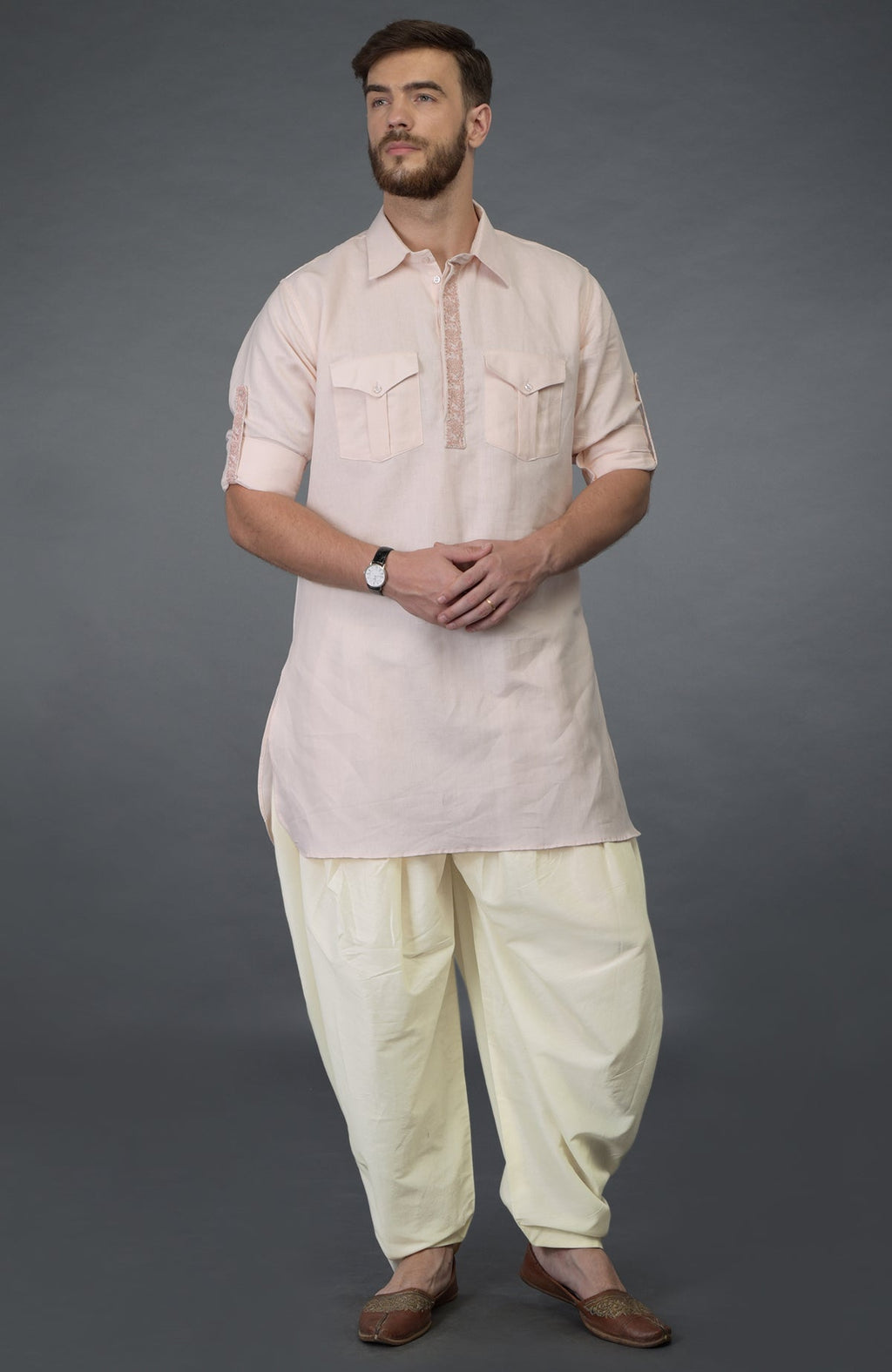 A man models a baby pink embroidered linen kurta set with ivory pathani salwar pants.