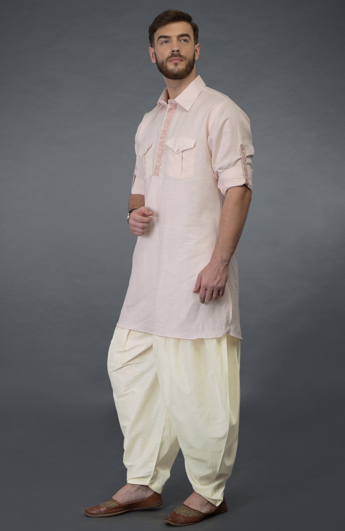 A man models a baby pink embroidered linen kurta set with ivory pathani salwar pants.