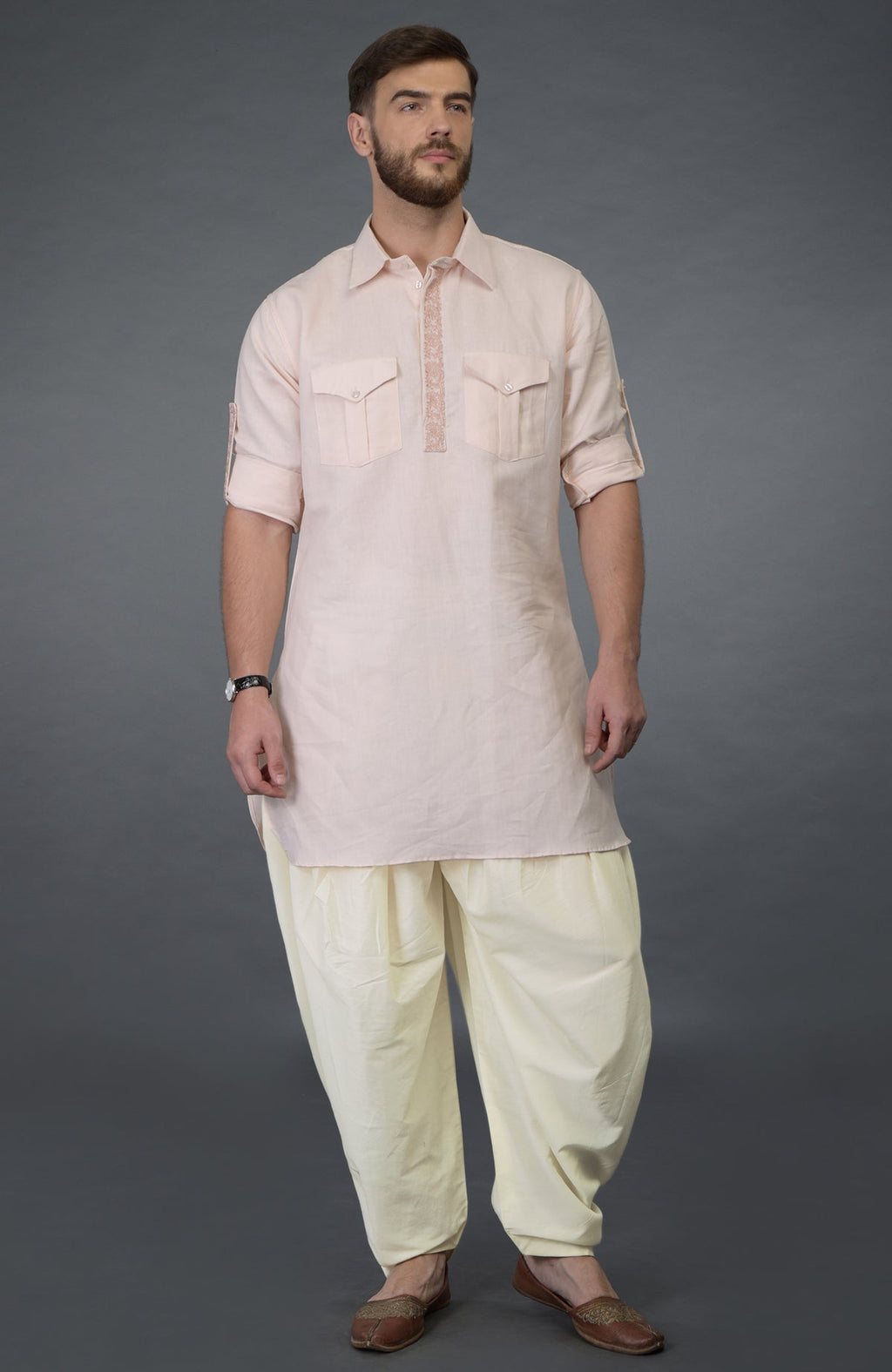 A man models a baby pink embroidered linen kurta set with ivory pathani salwar pants.
