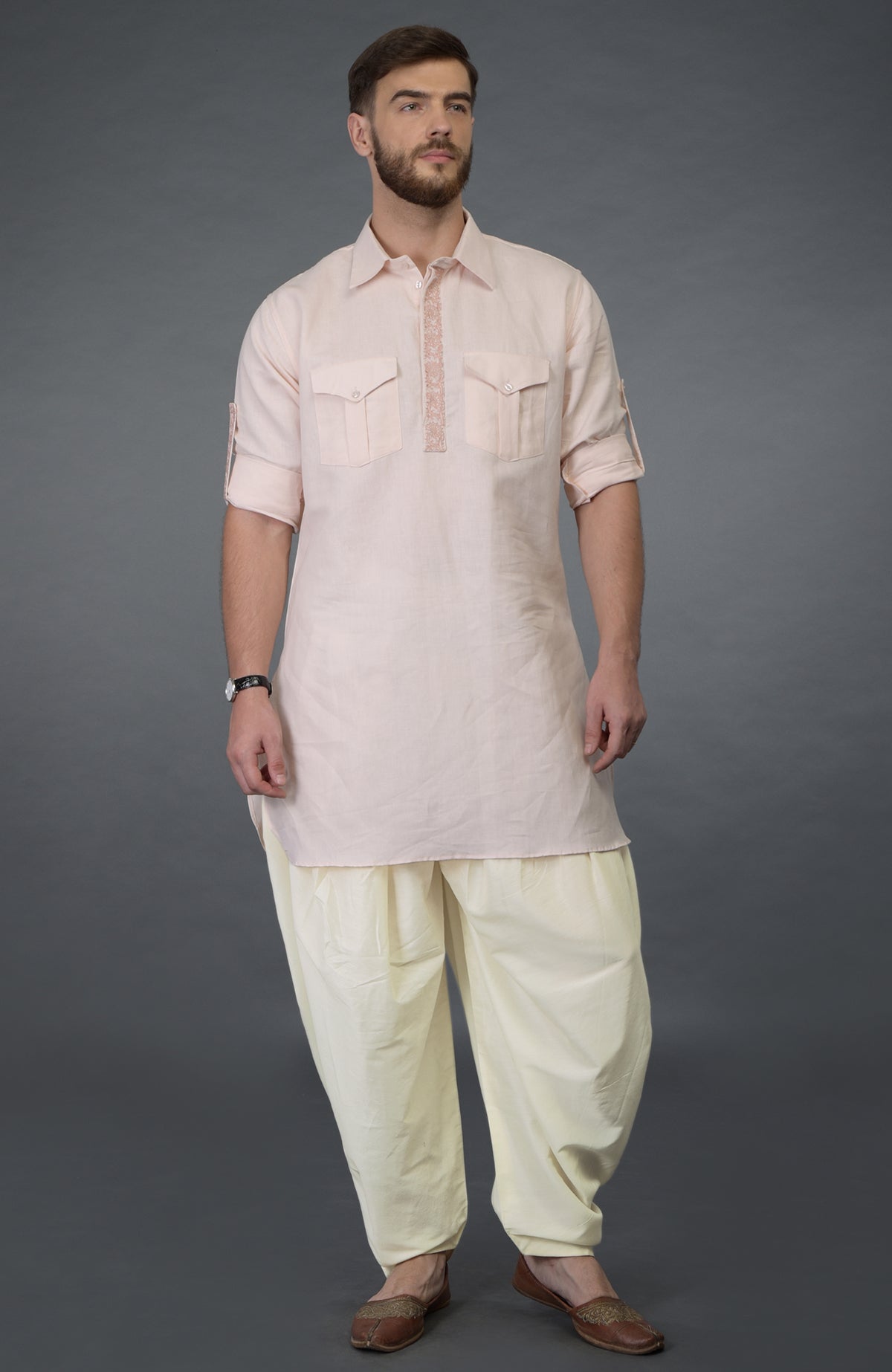 A man models a baby pink embroidered linen kurta set with ivory pathani salwar pants.