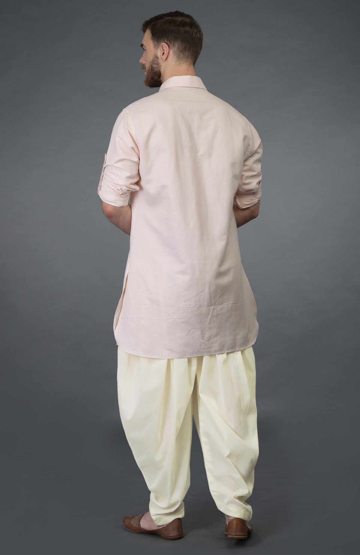 A man from behind wears a baby pink embroidered linen kurta and ivory pathani salwar pants.