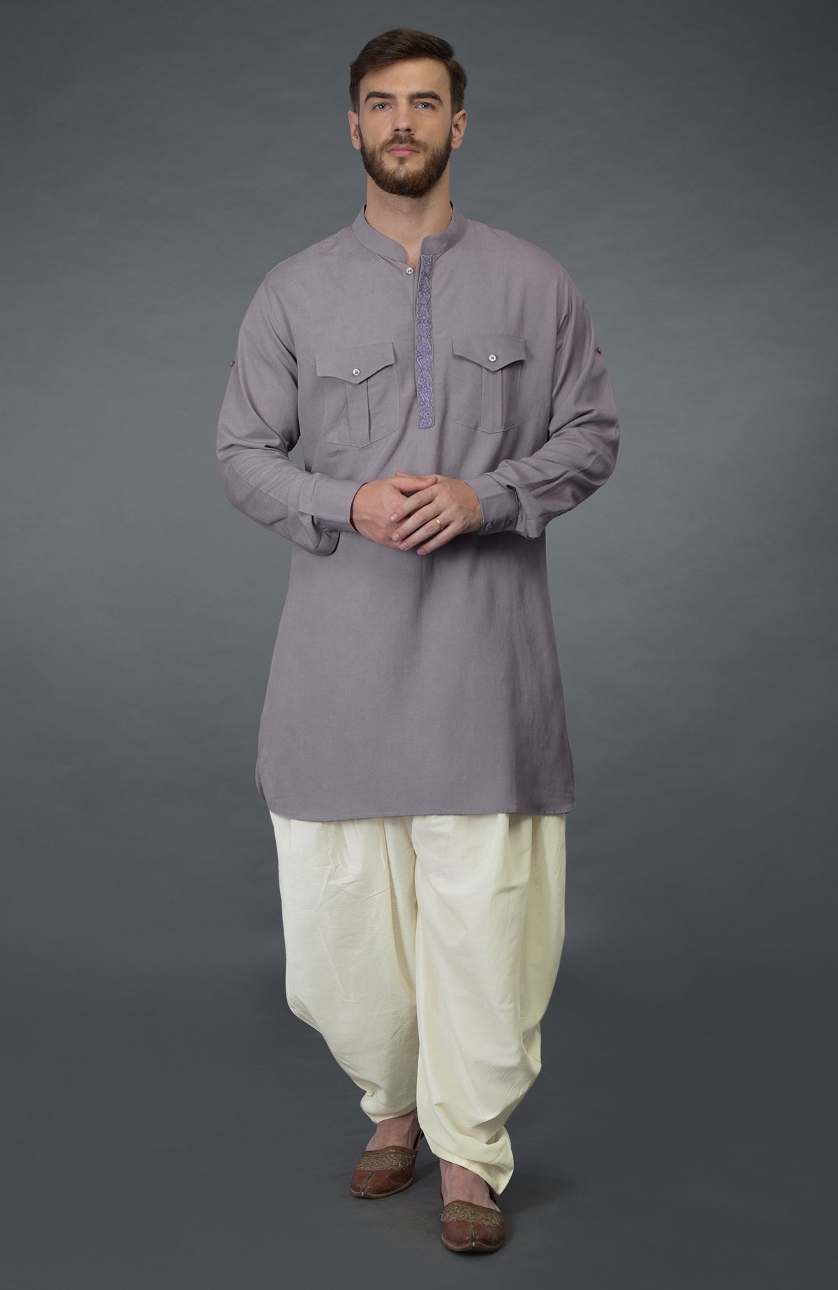 A man wears a lilac grey embroidered linen kurta set with ivory pathani salwar pants.