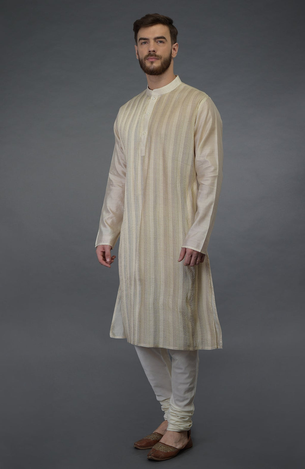 A man models a cream pintuck pure silk kurta set with matching churidar pants and brown juttis.