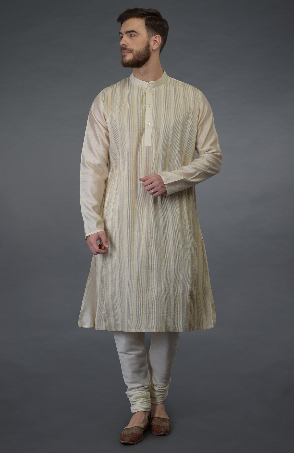 A man models a cream pure silk kurta with pintuck detail and cream churidar pants.