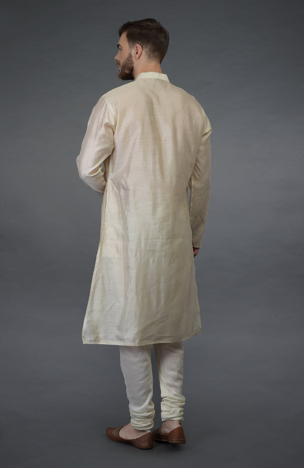 A man from behind wears a cream silk kurta set with brown shoes.