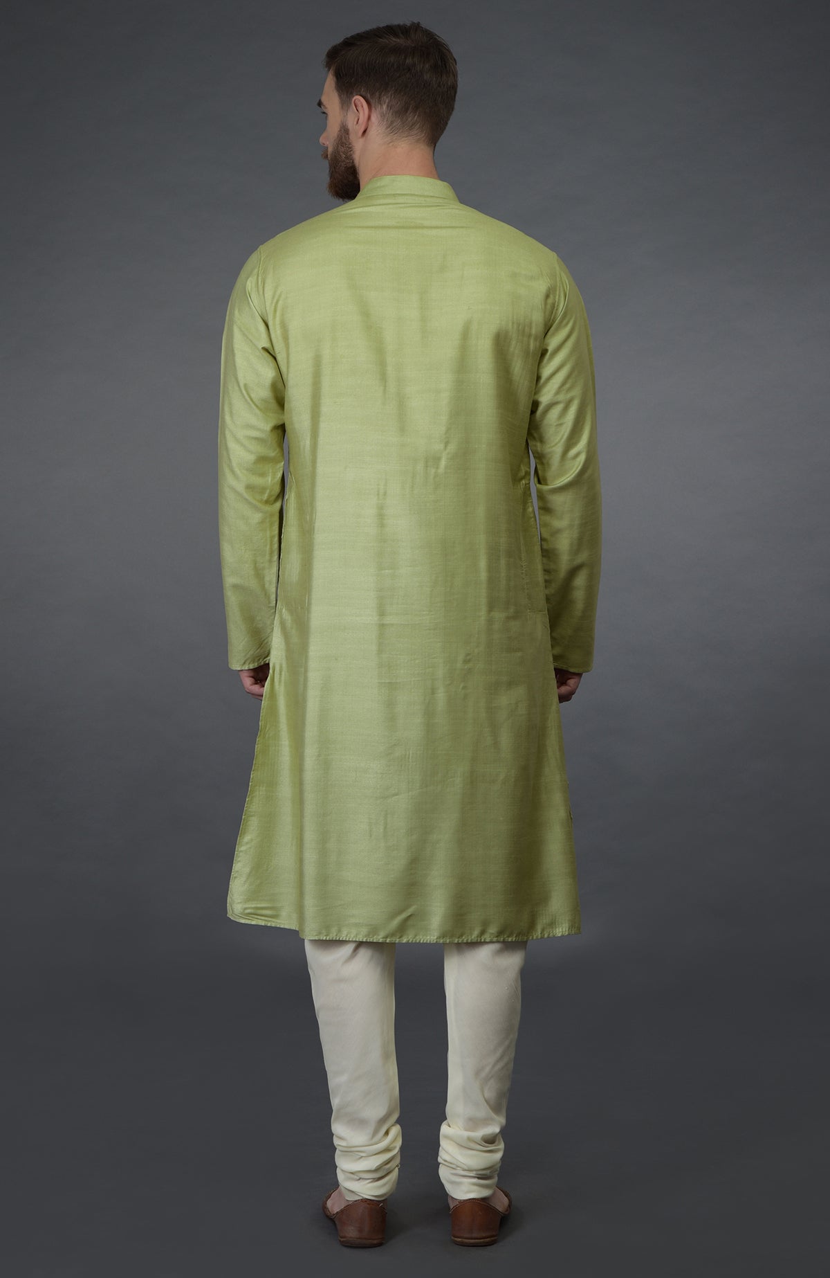 Pista green pintuck silk kurta with cream churidar pants and brown sandals.