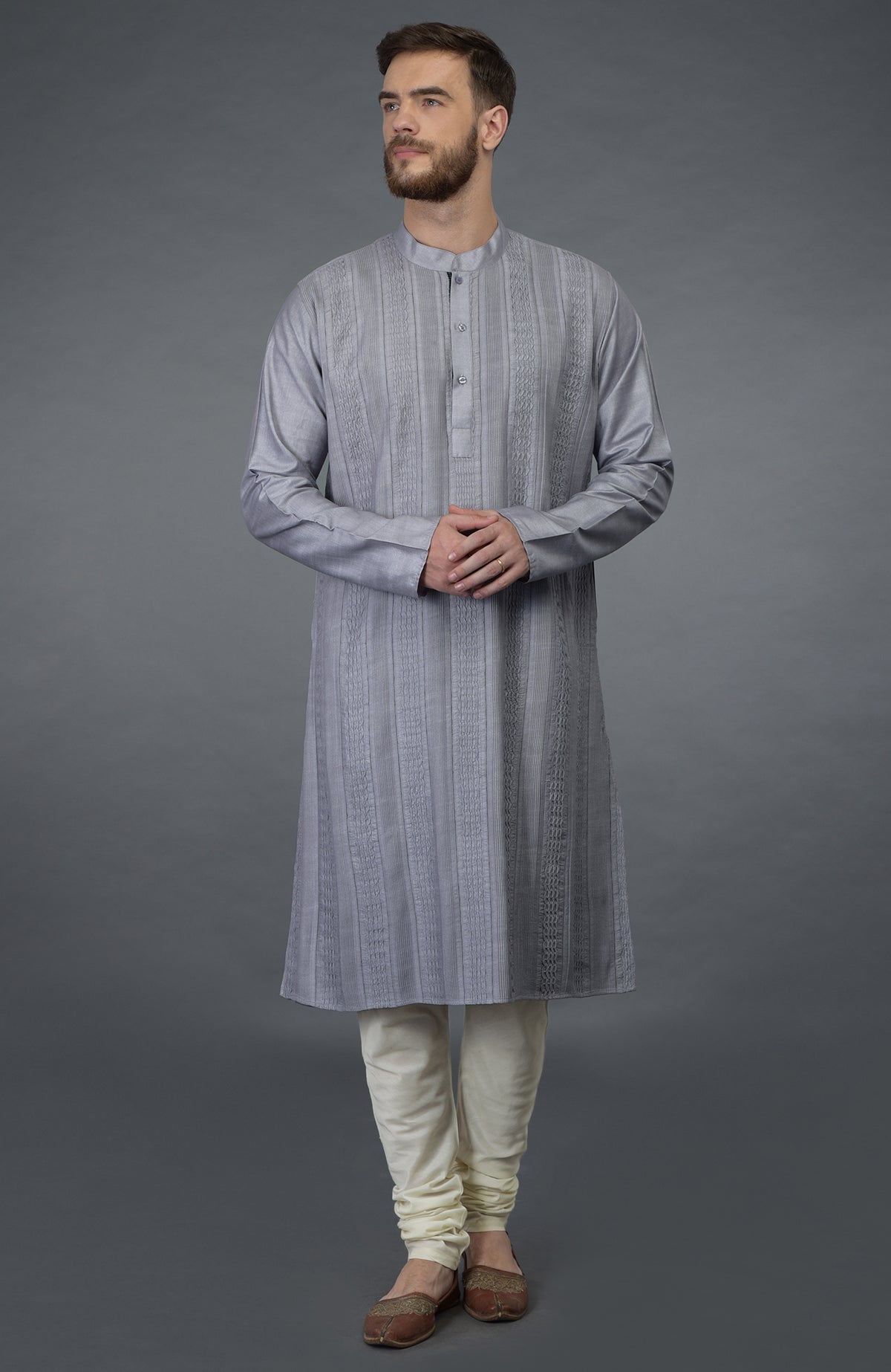 A man models a grey kurta with pintuck detail and ivory churidar pants.