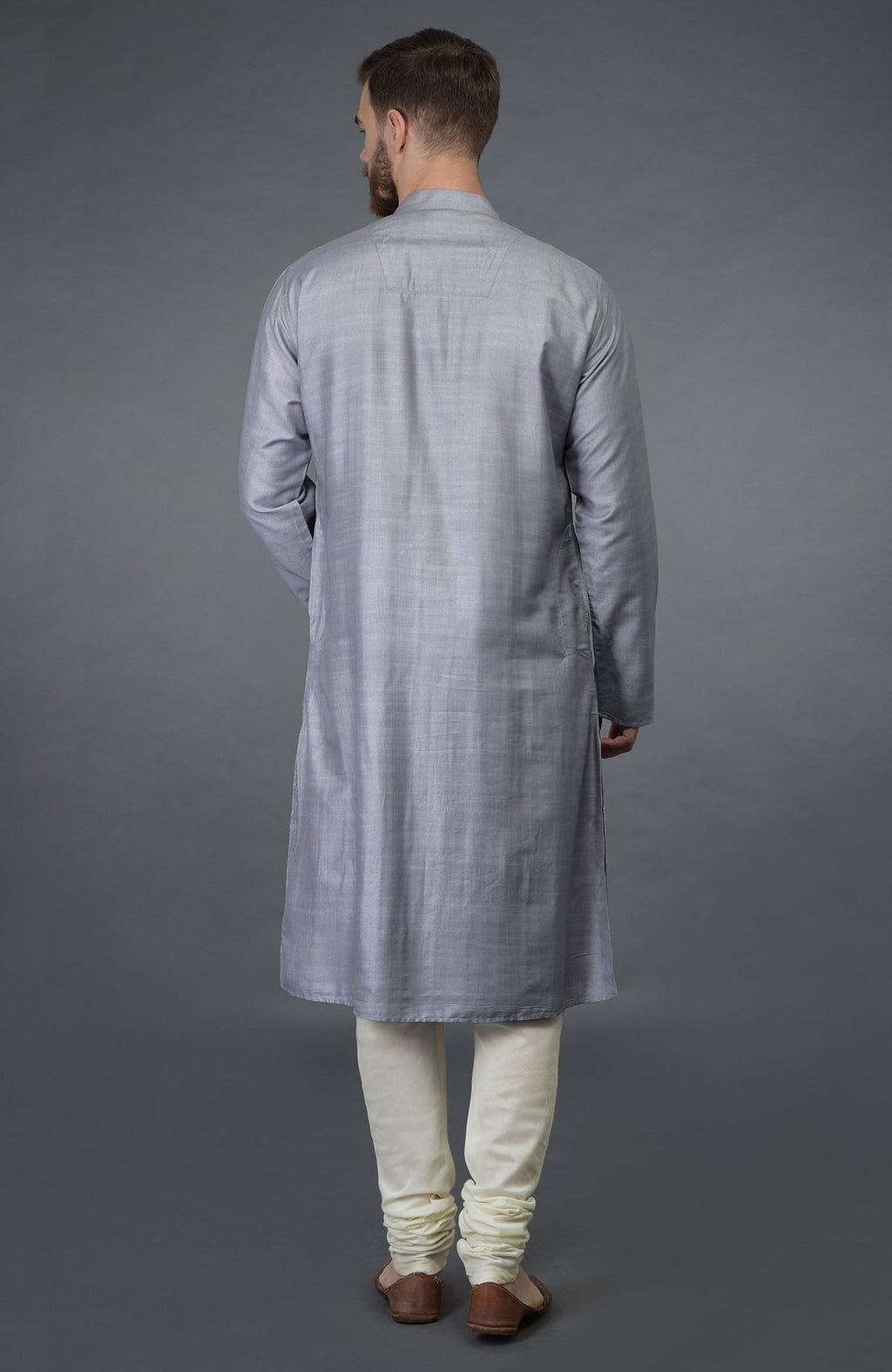 A man from behind wears a grey kurta with pintuck detail and ivory churidars.