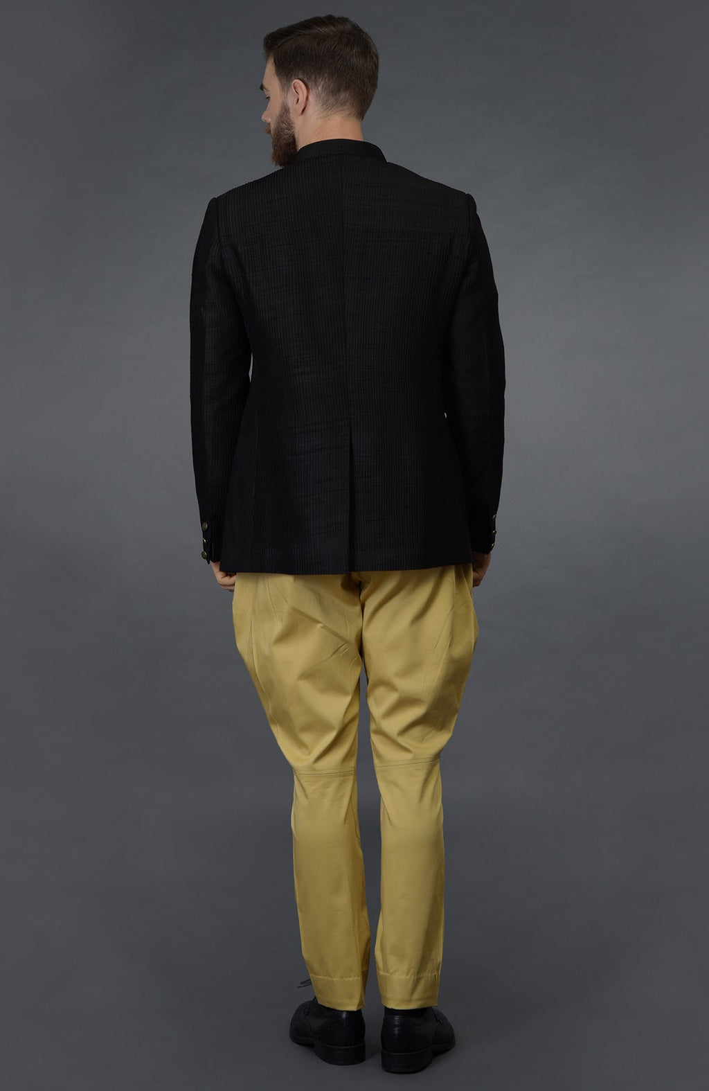 A man from behind wearing a black pintuck bandhgala jacket and camel beige breeches.